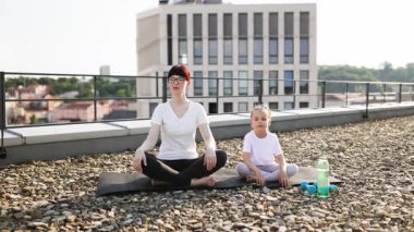 Kadın ve genç kız şehir çatısı üzerinde meditasyon yapıyorlar, farkındalık ve sükuneti ifade ediyorlar..