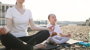 Anne yoga minderinde oturuyor ve kızıyla meditasyon yapıyor. Nilüfer pozisyonunda. Sağlıklı yaşam tarzının ardından sakin bir sabah atmosferinin tadını çıkarıyor.