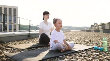 Anne ve kızı dışarıda Lotus pozisyonunda meditasyon yapıyorlar. Sabah ışığı altında çatı, huzurlu bir atmosfer yaratır. Zihinsel berraklığı, aile bağını, uygunluğu teşvik eder.