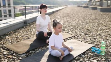 Anne ve kızı çatıda yoga yapıyor. Genç bir kadın ve kız dışarıda meditasyon yapıyor, sakin bir atmosfer. Aile bağı, yoga yaşam tarzı, sağlıklı yaşam..