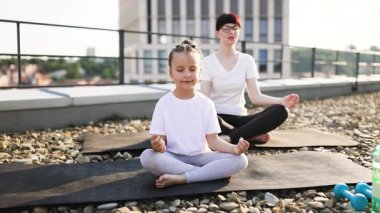 Anne ve kızı dışarıda Lotus pozisyonunda meditasyon yapıyorlar. Sabah ışığı altında çatı, huzurlu bir atmosfer yaratır. Zihinsel berraklığı, aile bağını, uygunluğu teşvik eder.