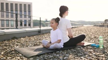 Kadın ve genç kız sabah vakti birlikte meditasyon yapıyorlar yoga minderlerinde yan yana oturuyorlar.