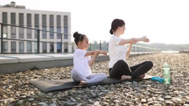 Anne ve kızı, güneşli bir günde çatıda spor yapıyor ve spor yapıyor. Spor kıyafetleri giyen kadın ve kız sağlıklı aile aktivitelerine girişiyor..