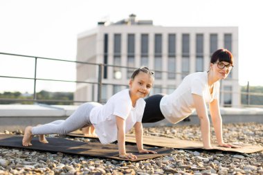 Anne ve kızı tahta egzersizleri yapıyor. Sağlıklı yaşam tarzı açık hava aktiviteleri ile vurgulandı.