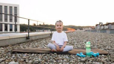 Lotus pozisyonunda oturan genç kız çatıda meditasyon yapıyor, farkındalık ve rahatlamaya odaklanıyor..