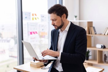 İş yerinde dizüstü bilgisayar kullanan takım elbiseli bir iş adamı. Modern ofis ortamı. Kendine güvenen yetişkin profesyonel erkek..