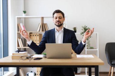 İş kıyafetleri içinde genç bir adam masa başında oturmuş, iş molası sırasında meditasyon yapıyordu. Sahne, işyerinin sağlığını, rahatlığını, farkındalığını vurguluyor. Kitap rafları olan ofis ortamı görünür bitki koltuğu
