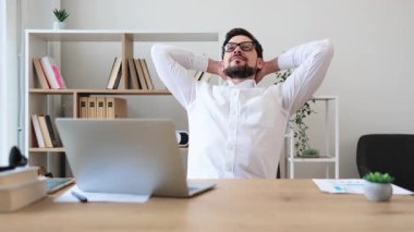 Genç, beyaz, gözlüklü, beyaz tişörtlü, ofis molasında gülümseyen, gevşeme ve pozitif iş hayatı dengesi gösteren genç bir erkek..