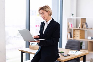 Modern parlak ofis ortamında dizüstü bilgisayarla çalışan kendine güvenen genç bir bayan profesyonel.