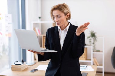 İş kadını resmi giysiler giyiyor. Modern ofis alanlarında dizüstü bilgisayarla çalışıyor.