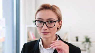Modern ofiste kendine güveni olan profesyonel bir kadın resmi takım elbise giyiyor. Masası, bitkileri ve arka planda rafları olan iş yeri. Başarı, profesyonellik ve motivasyonu temsil eder