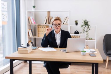 30 'lu yaşlarda kendine güvenen bir iş kadını parlak modern ofis ortamında masa başında çalışıyor.