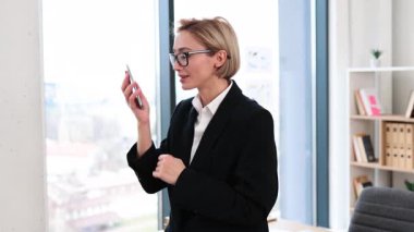 30 'lu yaşlarda kendine güvenen, resmi giyinmiş, şık ofis ortamında telefonla konuşan, arka planda masası ve rafları olan, iş başarısını ve iletişimini aktaran bir kadın.