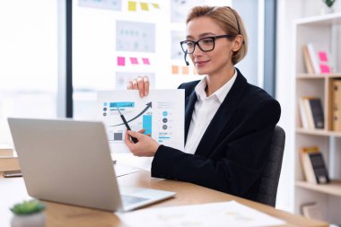 Otuzlu yaşlardaki iş kadını çevrimiçi toplantı sırasında dizüstü bilgisayar kullanarak finansal grafikler sunuyor, büyüme verilerini gösteriyor.