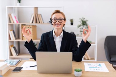 Genç beyaz kadın profesyonel dizüstü bilgisayar kullanıyor, çalışma alanındaki sakinliğini korurken meditasyon yapıyor. Dengeyi ve farkındalığı ifade etmek.