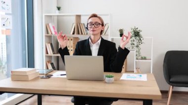 Genç beyaz kadın profesyonel dizüstü bilgisayar kullanıyor, çalışma alanındaki sakinliğini korurken meditasyon yapıyor. Dengeyi ve farkındalığı ifade etmek.