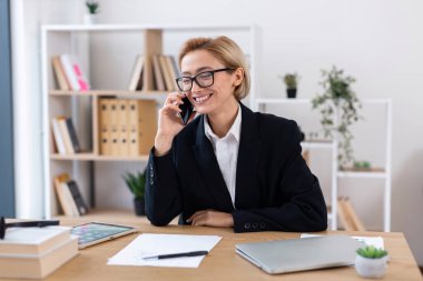 30 'lu yaşların ortasında iş kıyafeti giyen profesyonel bir kadın iş sırasında telefonla konuşuyor..