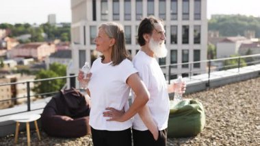 Antrenmandan sonra dışarıda duran yaşlı bir adam ve kadın ellerinde su şişeleri, spor giysileri giyiyorlar, fitness ve sağlıklı yaşam tarzlarını ifade ediyorlar..