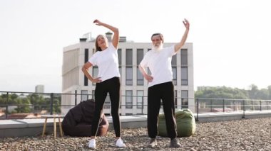 Yaşlı adam ve kadın yoga yapıyor ve şehir çatısı üzerinde esneme egzersizleri yapıyor..