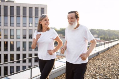 Üst düzey kadın ve erkek, açık çatı katında birlikte egzersiz yapıyorlar. Beyaz gömlekler giyiyorlar..