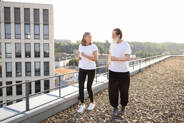 Sakallı yaşlı bir adam ve gündüz vakti şehrin çatısında koşan bir kadın. Yaşlı yetişkinler için aktif yaşam tarzı sağlık ve arkadaşlığı destekliyor.