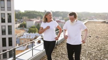 Üst düzey kadın ve erkek, açık çatı katında birlikte egzersiz yapıyorlar. Beyaz gömlekler giyiyorlar..