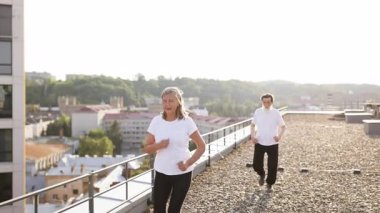 Aktif giyimli yaşlı kadın şehir çatısı üzerinde kollarını kaldırarak, dışarıda neşe ve canlılık ifade ediyor..