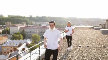 Üst düzey bir adam şehrin çatısında demiryolu ile yürüyor, orta yaşlı bir kadın arkadan koşuyor