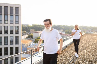 Üst düzey bir adam şehrin çatısında demiryolu ile yürüyor, orta yaşlı bir kadın arkadan koşuyor