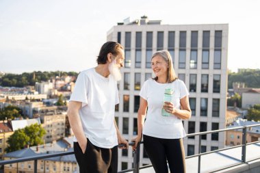 Yaşlı adam ve kadın günlük giysiler içinde şehrin çatısında egzersizden sonra dinleniyorlar.