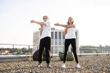 Üst düzey erkek ve kadın çatıda esneme egzersizleri yapıyor. Görüntü, denge esnekliği ve refahı vurgulayan yaşlı yetişkinler arasında fitness sağlıklı alışkanlıkları ve aktif yaşam tarzını teşvik eder.