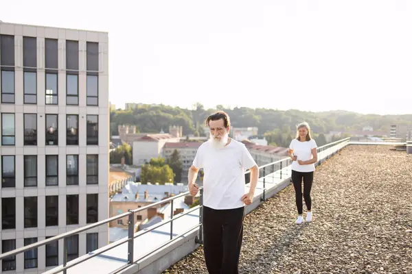 Aktif giyinmiş yaşlı adam ve kadın şehrin çatısı üzerinde koşuyorlar.
