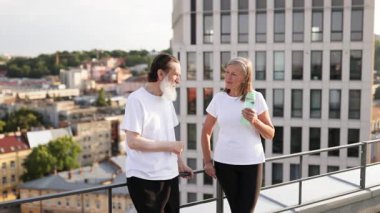 Yaşlı adam ve kadın günlük giysiler içinde şehrin çatısında egzersizden sonra dinleniyorlar.