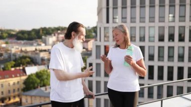 İki yaşlı yetişkin, erkek ve dişi, güneşli şehir merkezinde sabah egzersizlerinden sonra çatıda duruyorlar..