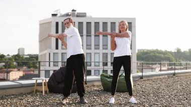 Üst düzey erkek ve kadın çatıda esneme egzersizleri yapıyor. Görüntü, denge esnekliği ve refahı vurgulayan yaşlı yetişkinler arasında fitness sağlıklı alışkanlıkları ve aktif yaşam tarzını teşvik eder.