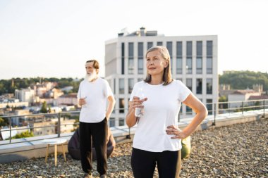 İki yetişkin, erkek ve dişi, idmandan sonra çatıda dinleniyorlar, ellerinde su şişeleri var..