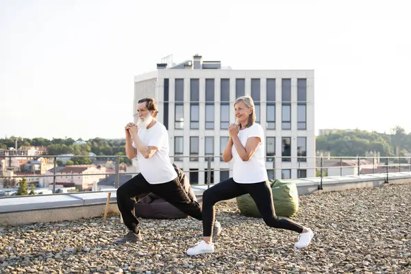 Yaşlı çift, güneşli bir sabahta çatıda yoga egzersizleri yaparak sağlık ve farkındalığı teşvik ediyorlar..