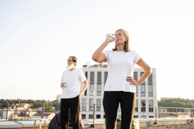 Yaşlı bir adam ve bir kadın açık çatı katında, şehir dışında idmandan sonra ferahlatıcı suyun tadını çıkarıyorlar. Sağlıklı yaşam tarzını, spor faaliyetlerini, aktif emekliliği ve sorumlu suyu temsil etmek