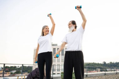 Üst düzey erkek ve kadın halterlerle dışarıda egzersiz yapıyor, fitness ve sağlıklı yaşam tarzını destekliyor..