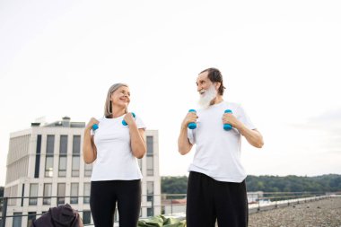 Yaşlı adam ve kadın şehir çatısı üzerinde dambıllarla sabah egzersizleri yapıyorlar..