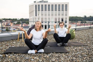 Lotus 'ta oturan yaşlı adam ve kadın, çatıda meditasyon yaparken poz veriyorlar..