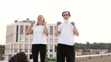 Yaşlı adam ve kadın şehir çatısı üzerinde dambıllarla sabah egzersizleri yapıyorlar..