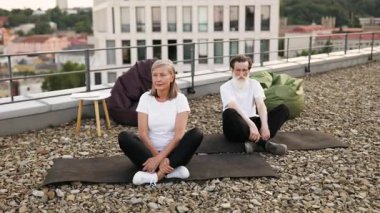 Lotus 'ta oturan yaşlı adam ve kadın, çatıda meditasyon yaparken poz veriyorlar..