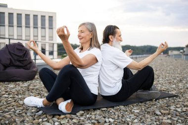 Yaşlı bir kadın çatıda oturmuş meditasyon yoga nilüfer pozu çalışıyor. Sağlıklı yaşam tarzı fitness açık hava aktiviteleri farkındalık sağIık rahatlama dengesi eşleştirilmiş egzersiz
