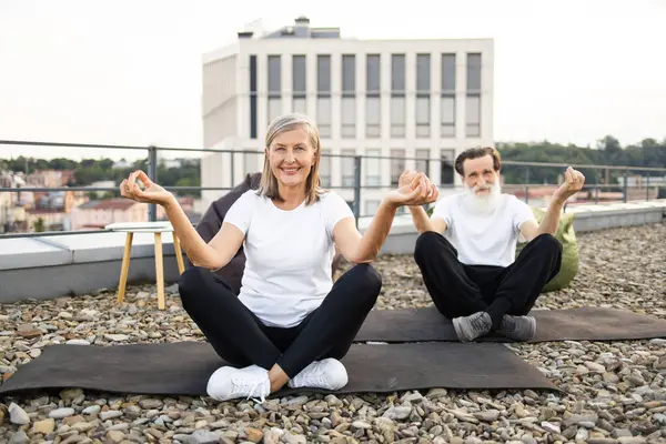 Üst düzey erkek ve kadın dışarıda terasta nilüfer çiçeğiyle yoga yapıyorlar..