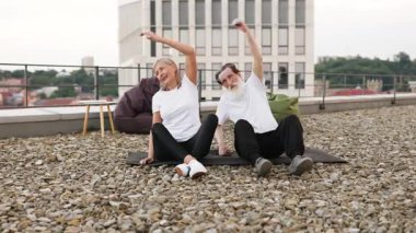 Yaşlı bir adam ve kadın birlikte egzersiz yapıyor, dışarıda yoga yaparken kollarını esnetiyorlar. Sağlıklı yaşam tarzı, canlılık, açık hava egzersizi terasta olgun yetişkinler için esneklik ve gevşemeyi teşvik ediyor.