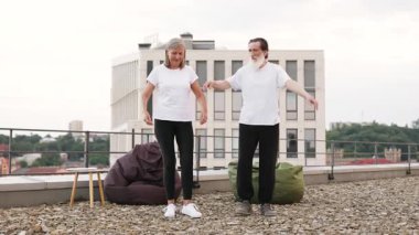 Yaşlı bir adam ve kadın, şehrin çatısında yoga egzersizi yapıyorlar. Sağlıklı yaşam tarzı, zindelik.