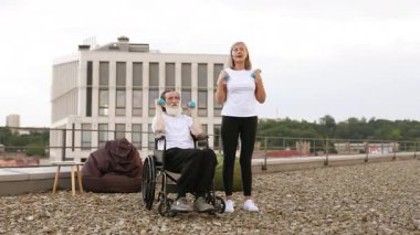 Tekerlekli sandalyedeki son sınıf öğrencisi ve şehir çatılarında dambıllarıyla egzersiz yapan aktif yaşam tarzlarını destekleyen kadın. Cesaret, birliktelik, sağlık, canlılık ve fitness desteği