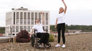 Yaşlı bir çift, kadın esneme hareketleri, tekerlekli sandalyedeki bir adam dışarıda kollarını kaldırıyor. Takım çalışması, destek, aktif yaşam tarzı, maluliyet bilinci, karşılıklı teşvik, açık hava egzersiz ayarları.