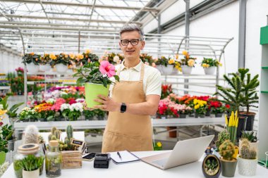 Kafkasyalı bir erkek çiçekçi elinde satılık bir saksı bitkisi olan bir dükkanda duruyor..